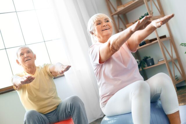 Senior couple exercise together at home doing aerobics hands in front